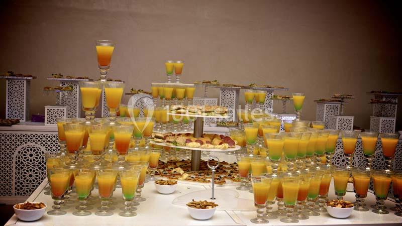 Table garnie de verres de jus colorés, de pâtisseries et de petits bols, disposés pour un buffet élégant.