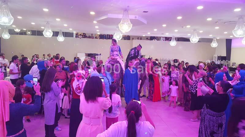 Des personnes rassemblées dans une salle festive, entourant deux individus assis sur des chevaux décorés.