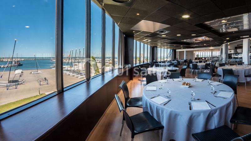 Salle de restaurant lumineuse avec grandes baies vitrées offrant une vue sur un port de plaisance et des voiliers.