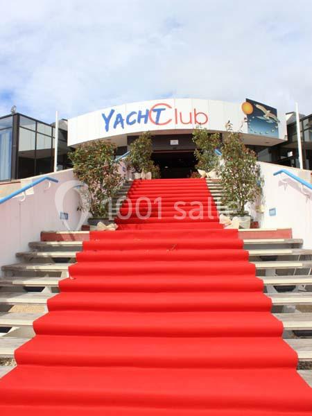 Escalier couvert d'un tapis rouge menant à l'entrée d'un bâtiment avec une enseigne ’Yacht Club’.