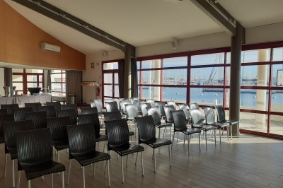 Terrasse d'un restaurant en bois avec vue sur un port de plaisance, tables occupées et végétation en premier plan.
