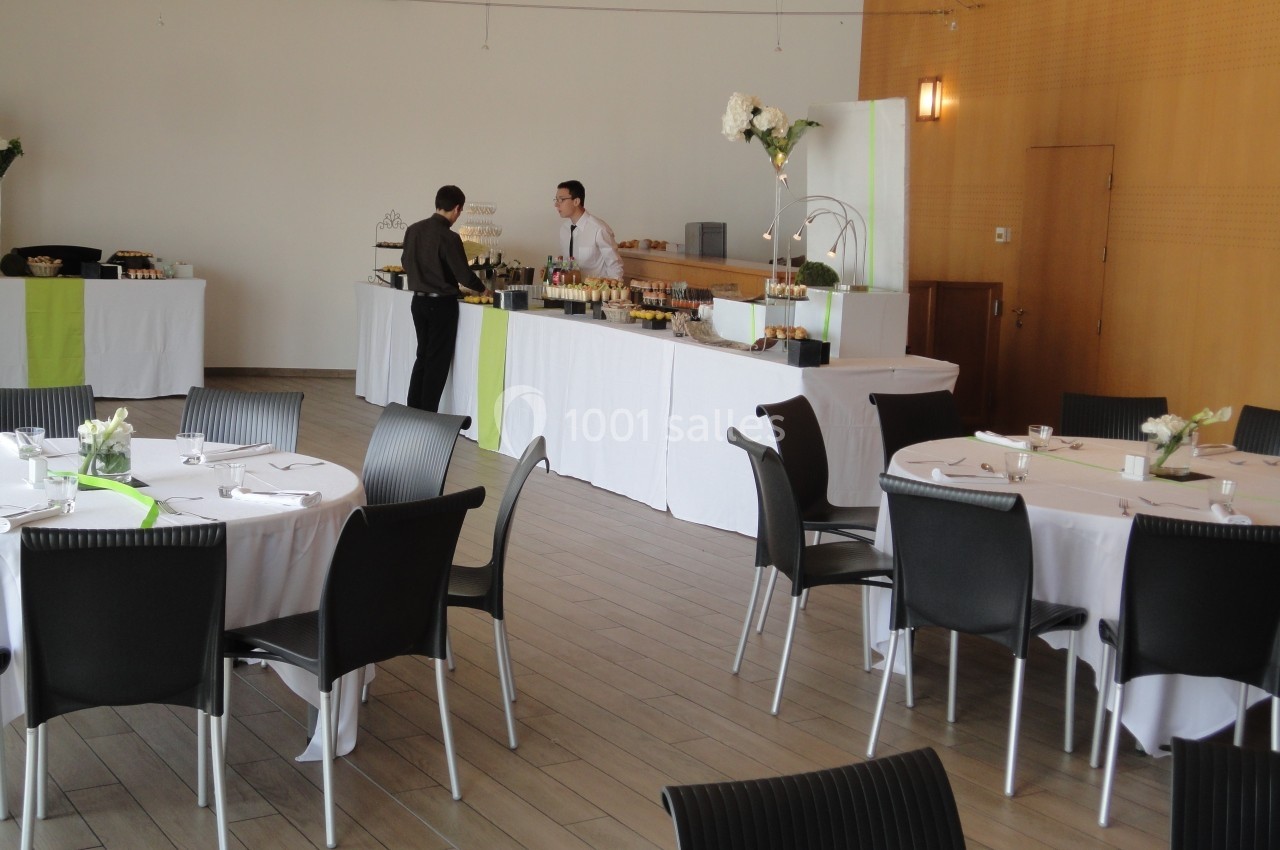 Salle de réception avec tables dressées et un buffet où deux personnes discutent près du comptoir.