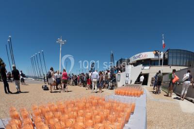 Terrasse d'un restaurant en bois avec vue sur un port de plaisance, tables occupées et végétation en premier plan.