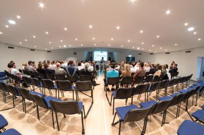 Terrasse d'un restaurant en bois avec vue sur un port de plaisance, tables occupées et végétation en premier plan.