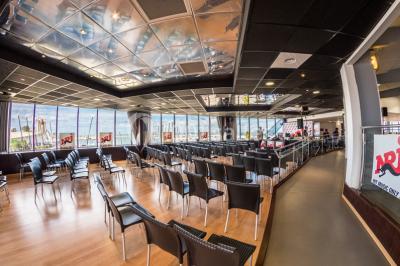 Terrasse d'un restaurant en bois avec vue sur un port de plaisance, tables occupées et végétation en premier plan.