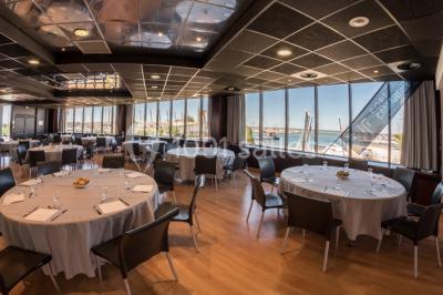 Terrasse d'un restaurant en bois avec vue sur un port de plaisance, tables occupées et végétation en premier plan.