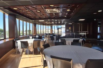 Terrasse d'un restaurant en bois avec vue sur un port de plaisance, tables occupées et végétation en premier plan.
