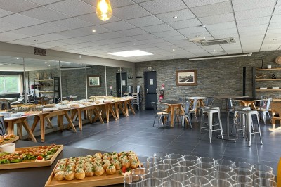 Salle lumineuse avec tables en bois, chaises noires, sol en carrelage sombre et murs en pierre.