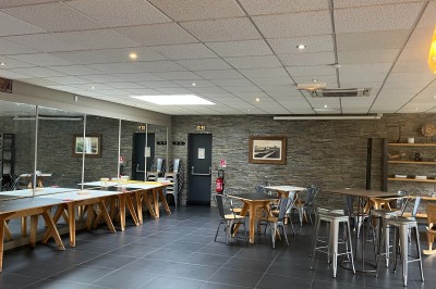 Salle lumineuse avec tables en bois, chaises noires, sol en carrelage sombre et murs en pierre.