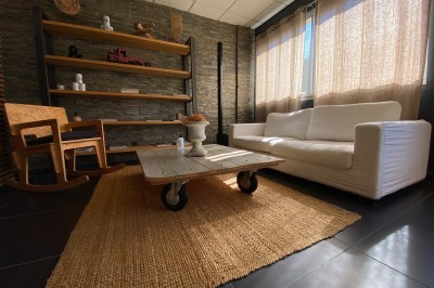 Salle lumineuse avec tables en bois, chaises noires, sol en carrelage sombre et murs en pierre.