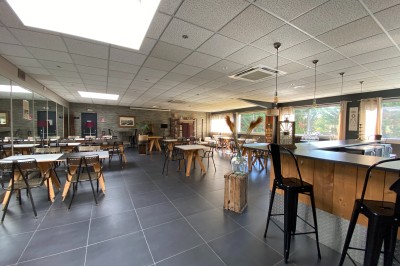 Salle lumineuse avec tables en bois, chaises noires, sol en carrelage sombre et murs en pierre.