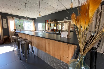 Salle lumineuse avec tables en bois, chaises noires, sol en carrelage sombre et murs en pierre.