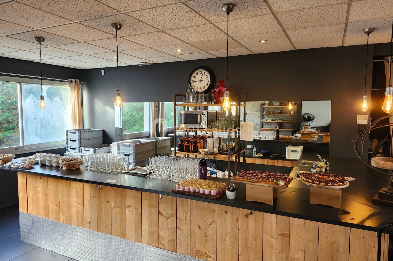 Comptoir en bois dans une salle moderne, avec verrerie, plateaux de nourriture et éclairage suspendu.