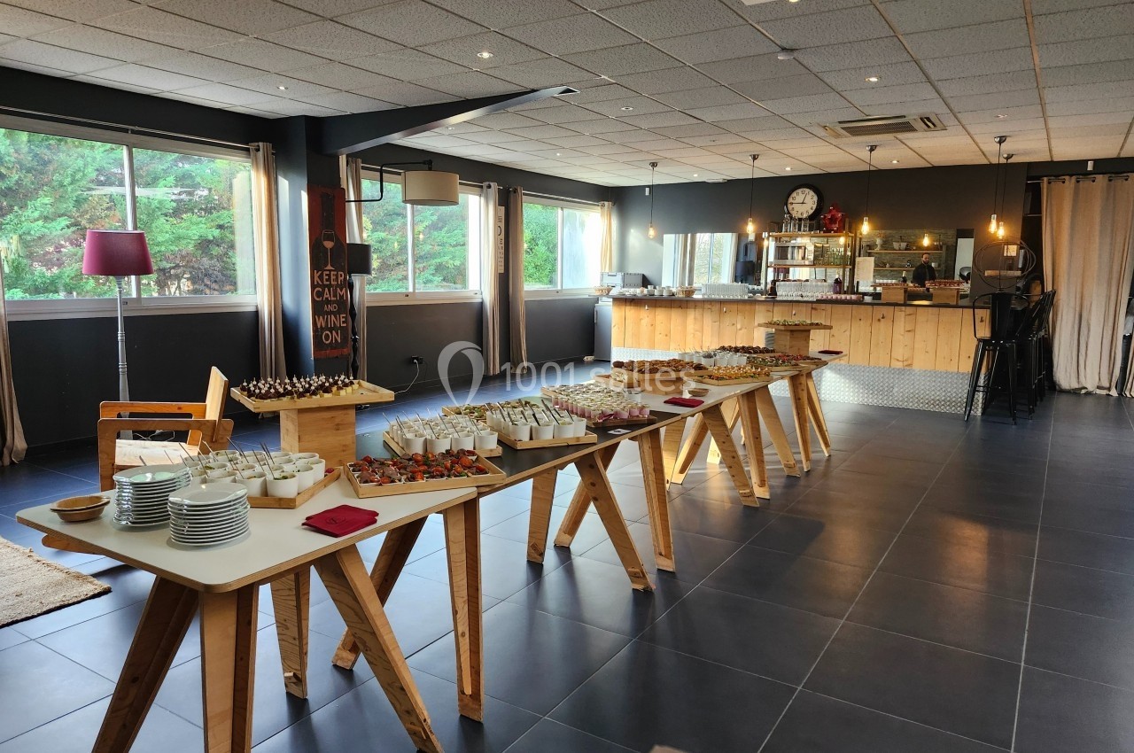Salle lumineuse avec tables en bois disposées pour un buffet, contenant divers plats et verrines.