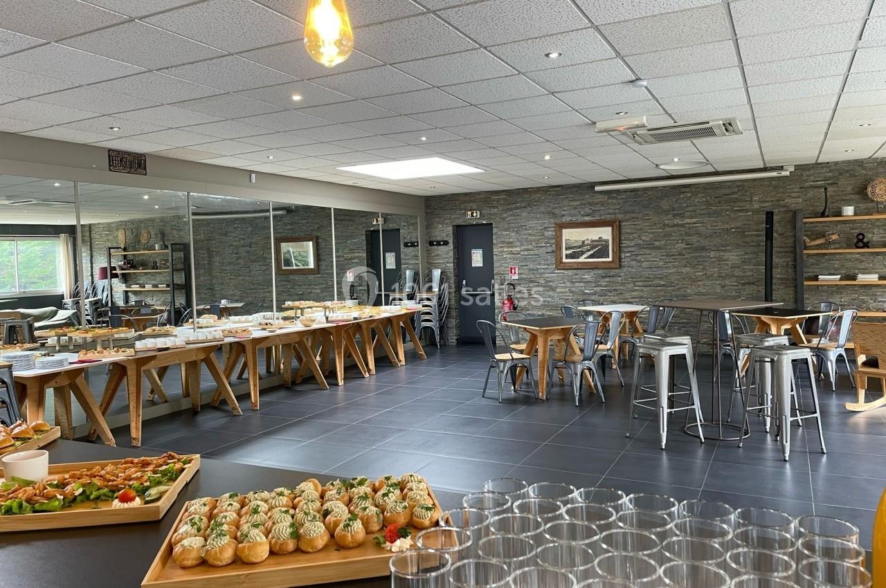 Salle de réception moderne avec tables dressées pour un buffet, décorée de murs en pierre et éclairée par des suspensions.