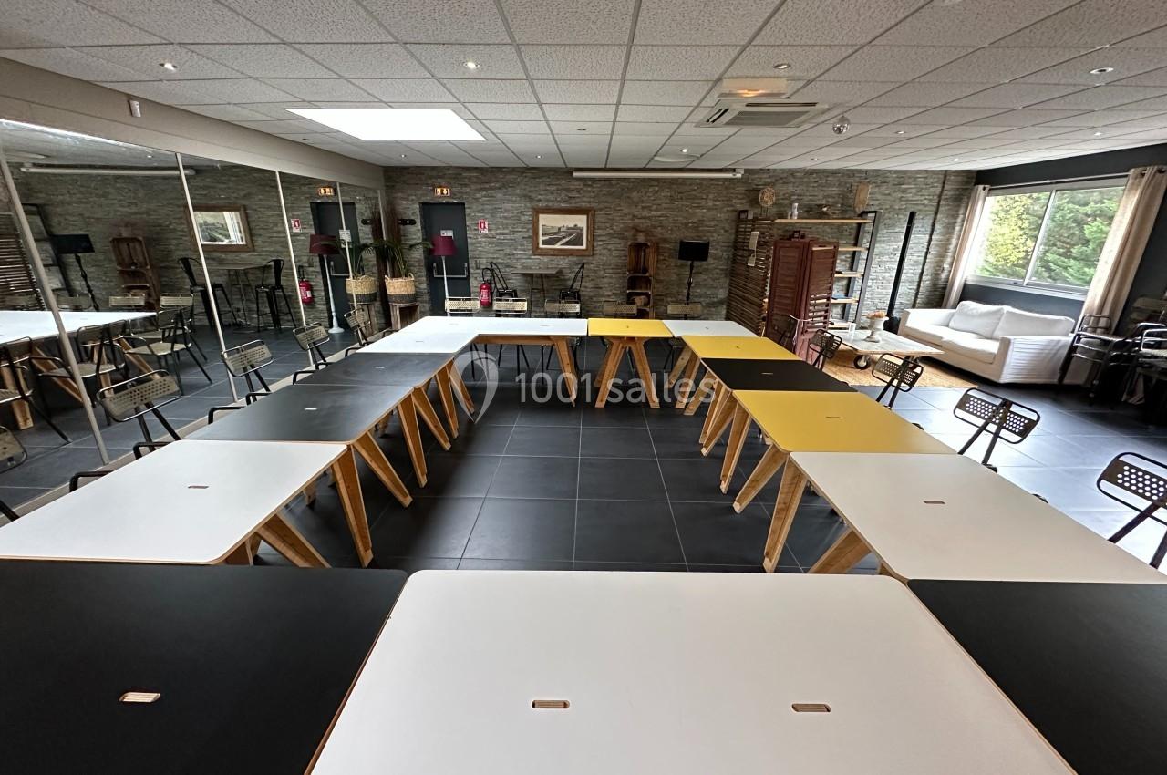 Salle de réunion avec des tables disposées en U, chaises noires, murs en pierre et grandes fenêtres laissant entrer la…