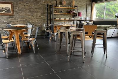 Salle moderne avec tables colorées en bois, chaises métalliques, grand miroir et comptoir en arrière-plan.