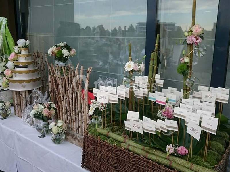 Table décorative avec compositions florales, présentoirs en bambou et étiquettes nominatives, devant une vitre.