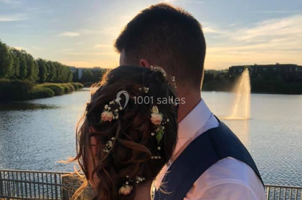Un couple de dos près d'un lac au coucher du soleil, avec des fleurs dans les cheveux de la femme.