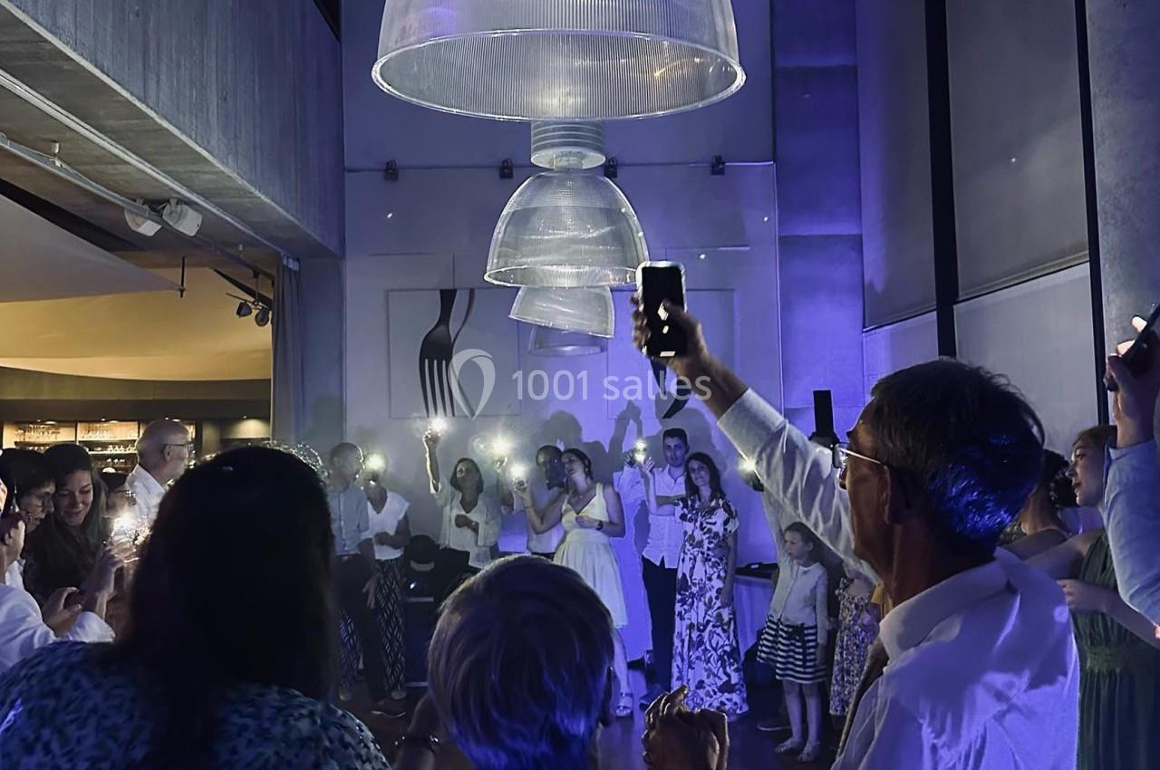 Des personnes rassemblées dans une salle sombre, éclairées par des lumières de téléphones et des lampes suspendues.