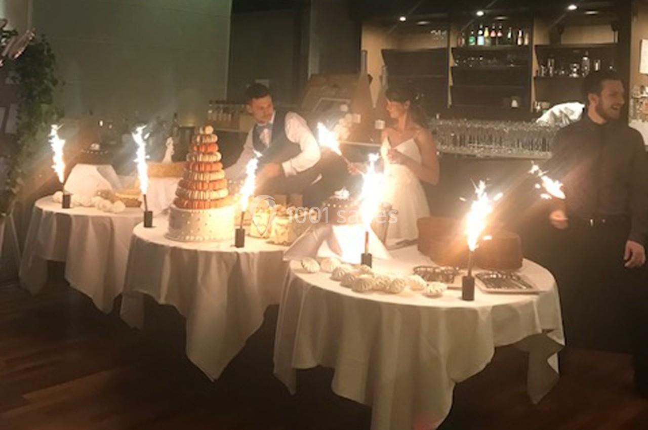 Des tables décorées avec des desserts, des fontaines lumineuses et des convives en tenue de fête dans une salle éclairée.