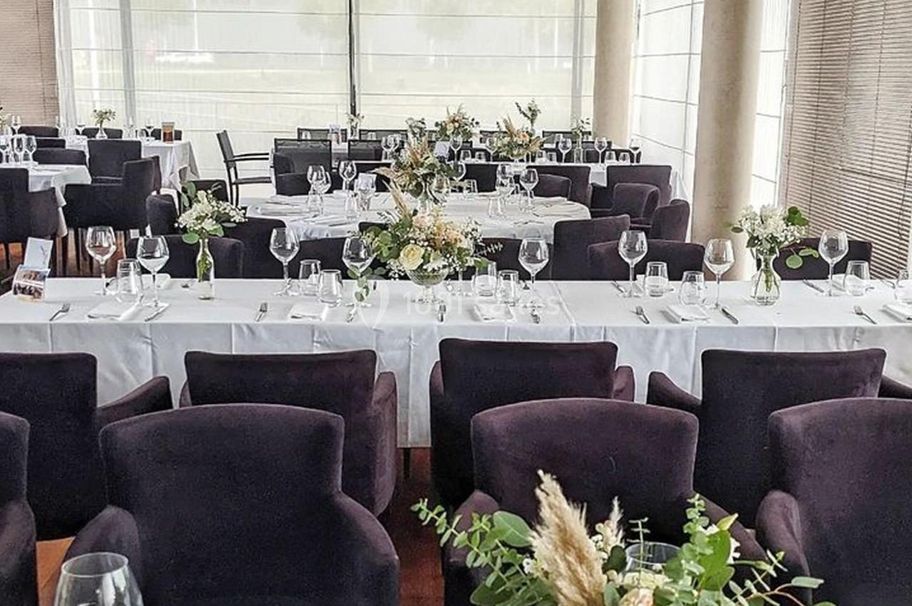 Salle de réception avec tables dressées, nappes blanches, verres, couverts et décorations florales élégantes.