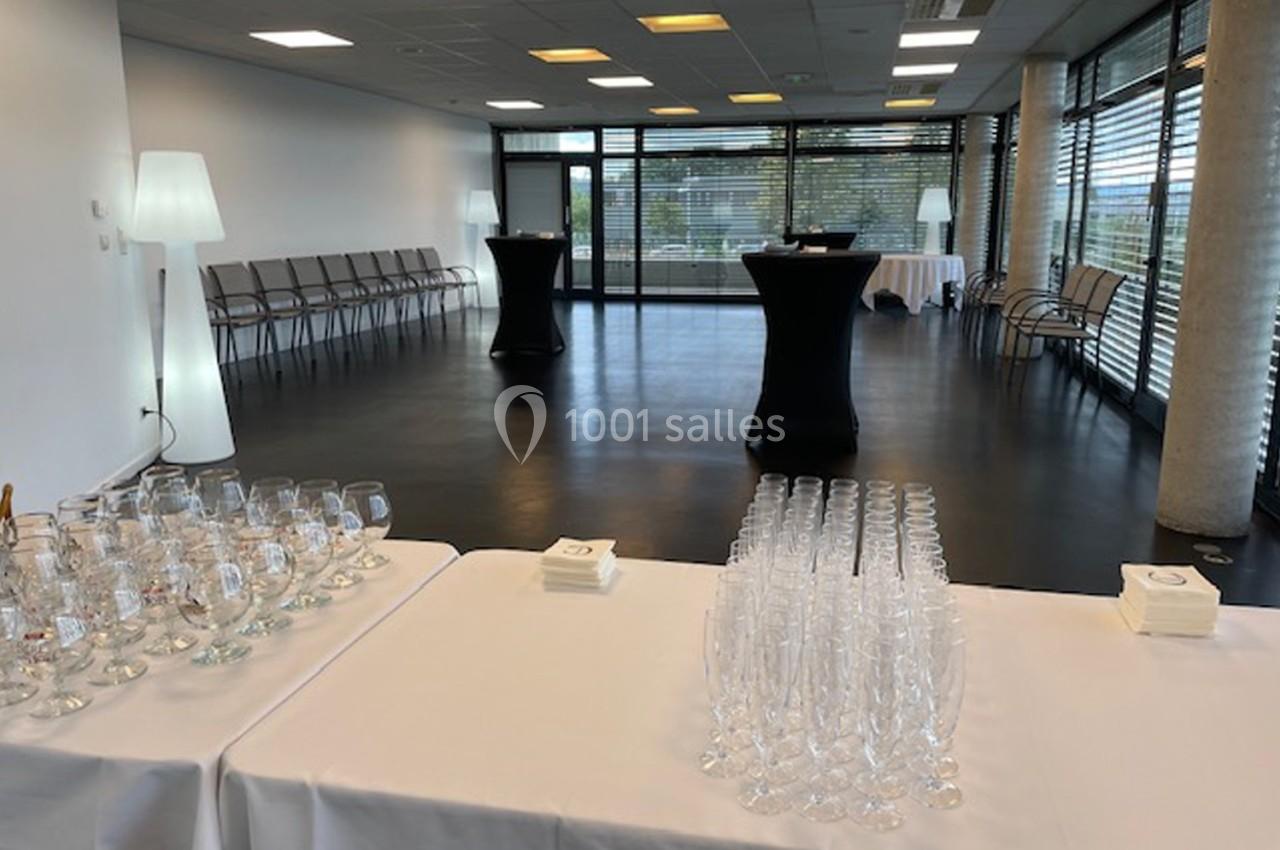 Salle lumineuse avec tables dressées pour un événement, verres et serviettes disposés au premier plan.
