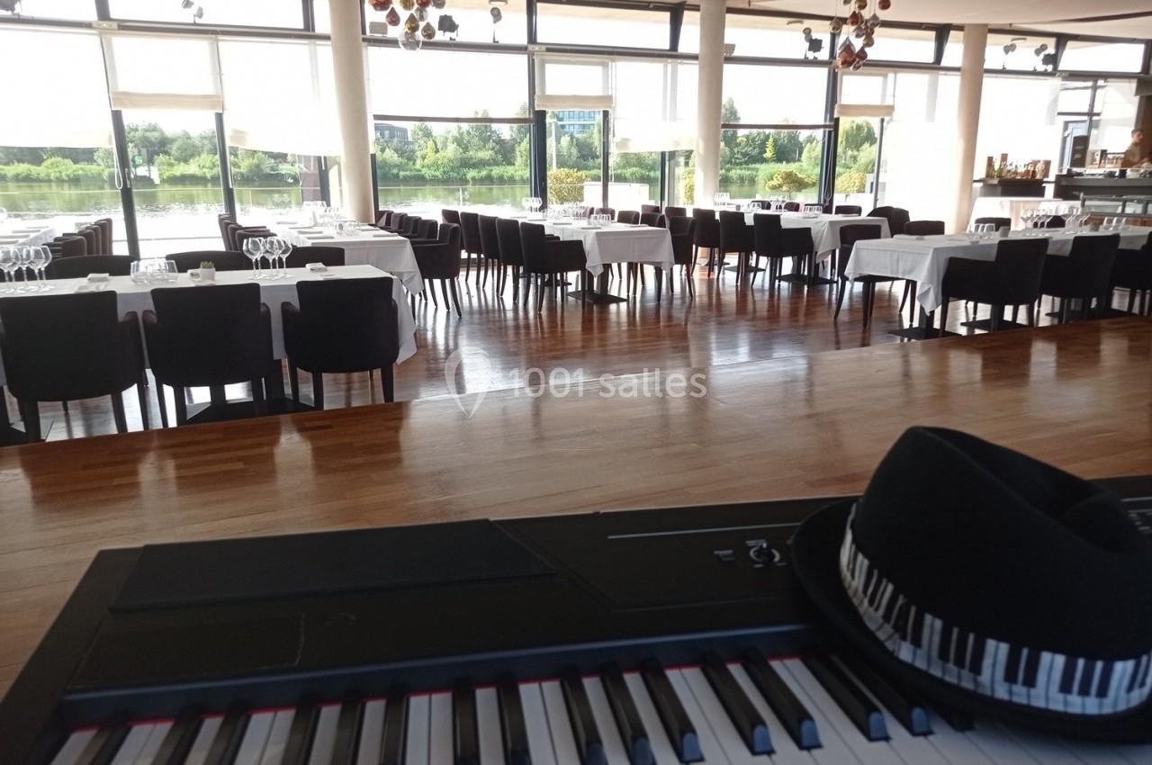Salle de restaurant lumineuse avec des tables dressées, vue sur un piano et un chapeau posé dessus au premier plan.