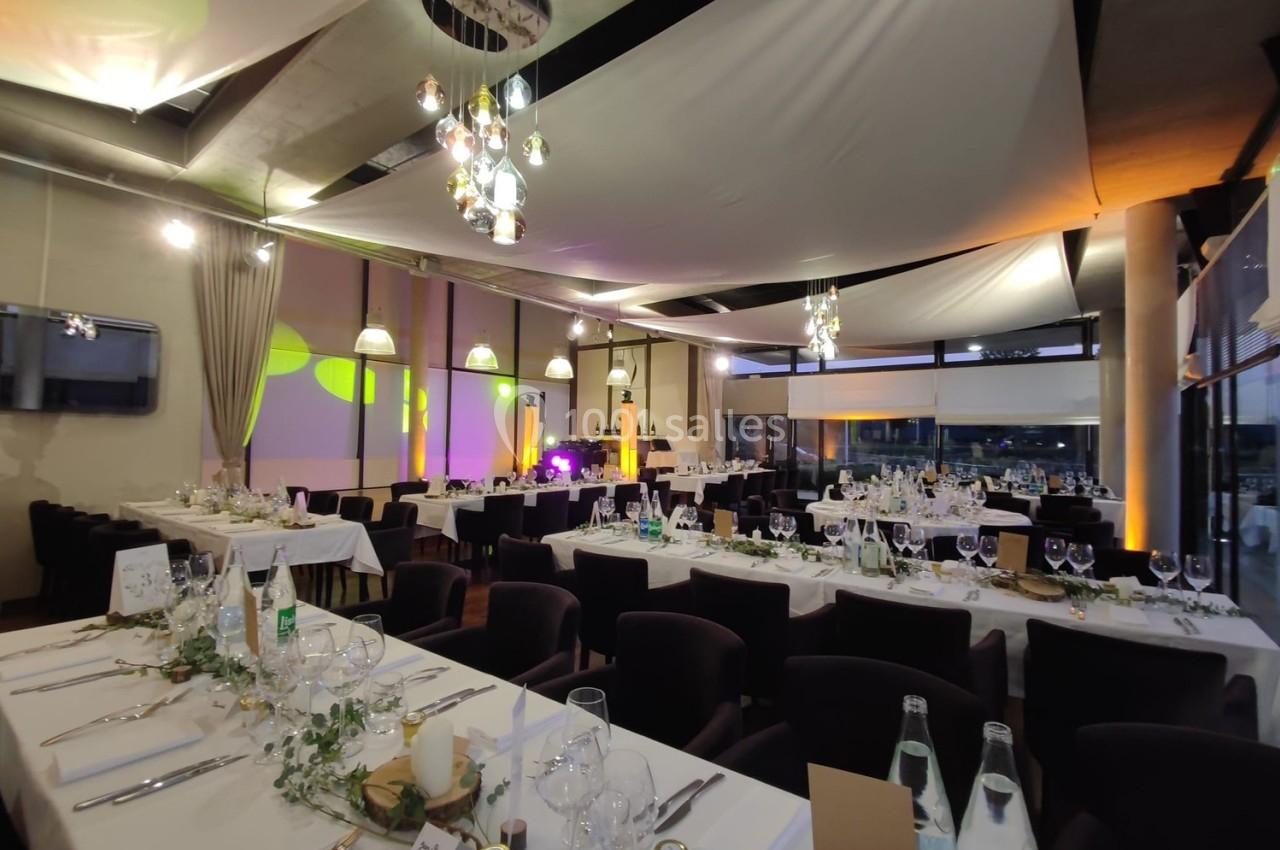 Salle de réception décorée pour un événement, avec tables dressées, éclairage tamisé et ambiance élégante.