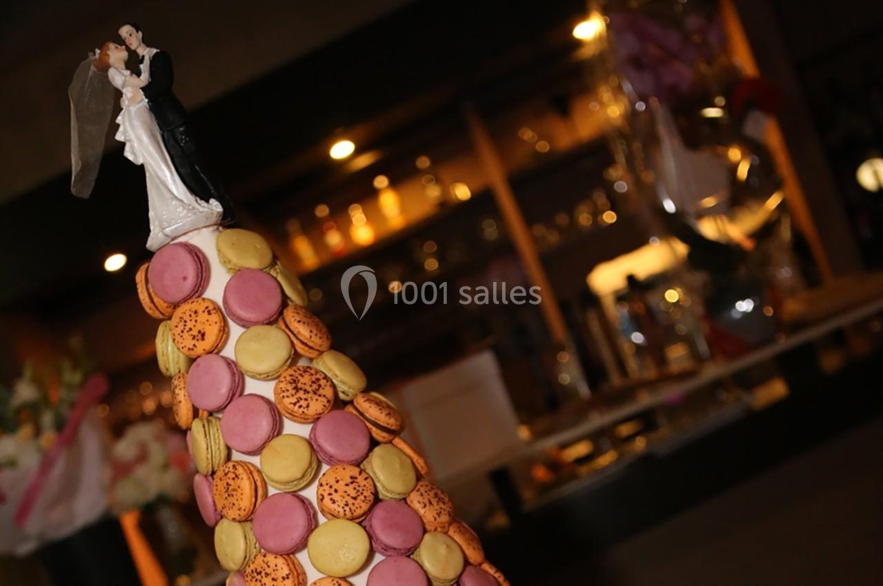 Figurine de mariés au sommet d'une pièce montée décorée de macarons colorés, avec un arrière-plan flou de bar.