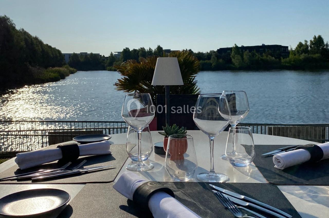 Table dressée avec élégance en extérieur, vue sur un lac ensoleillé et végétation en arrière-plan.