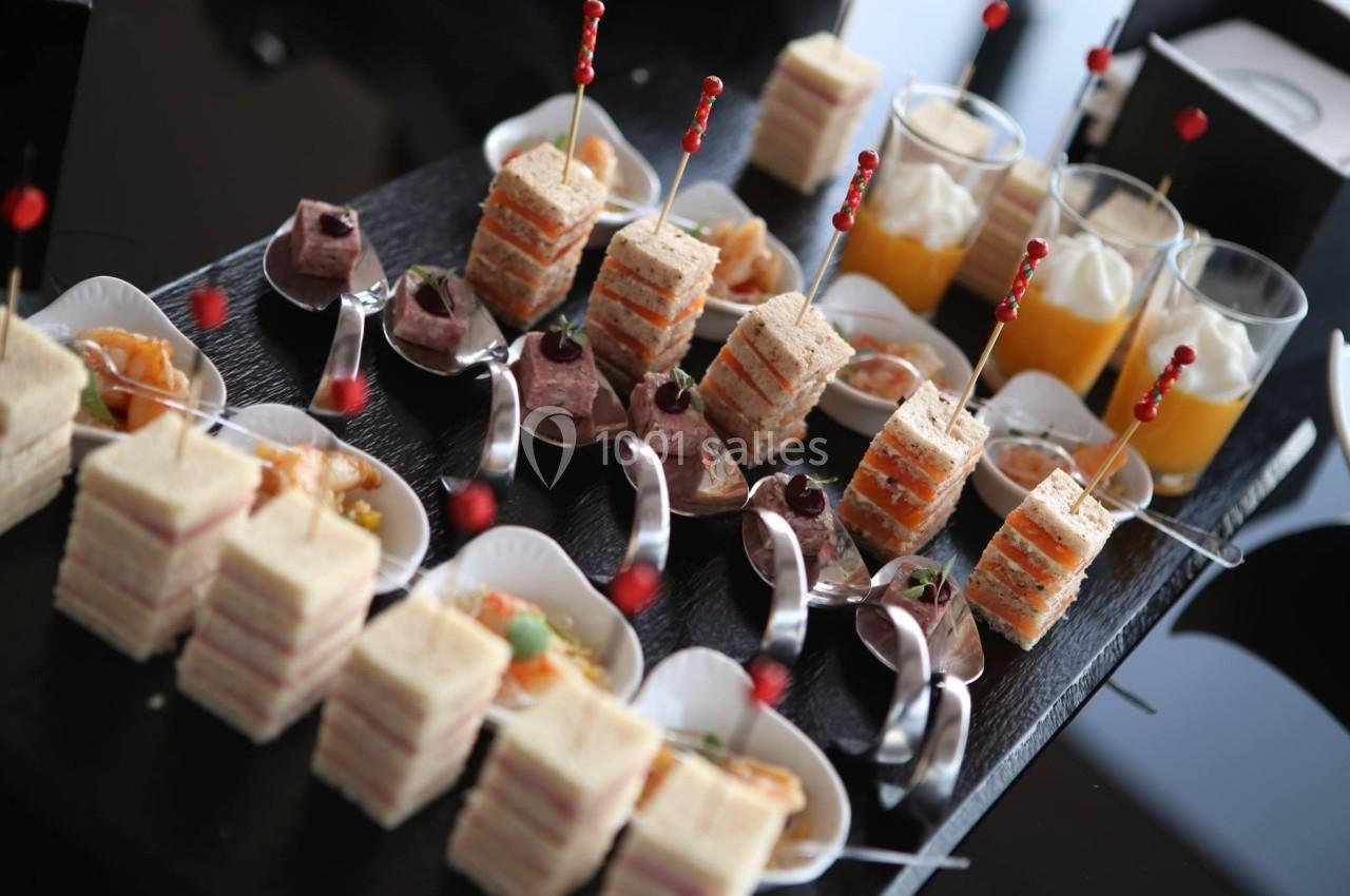 Plateau de bouchées apéritives comprenant mini-sandwichs, verrines et cuillères garnies, présenté sur une table noire.