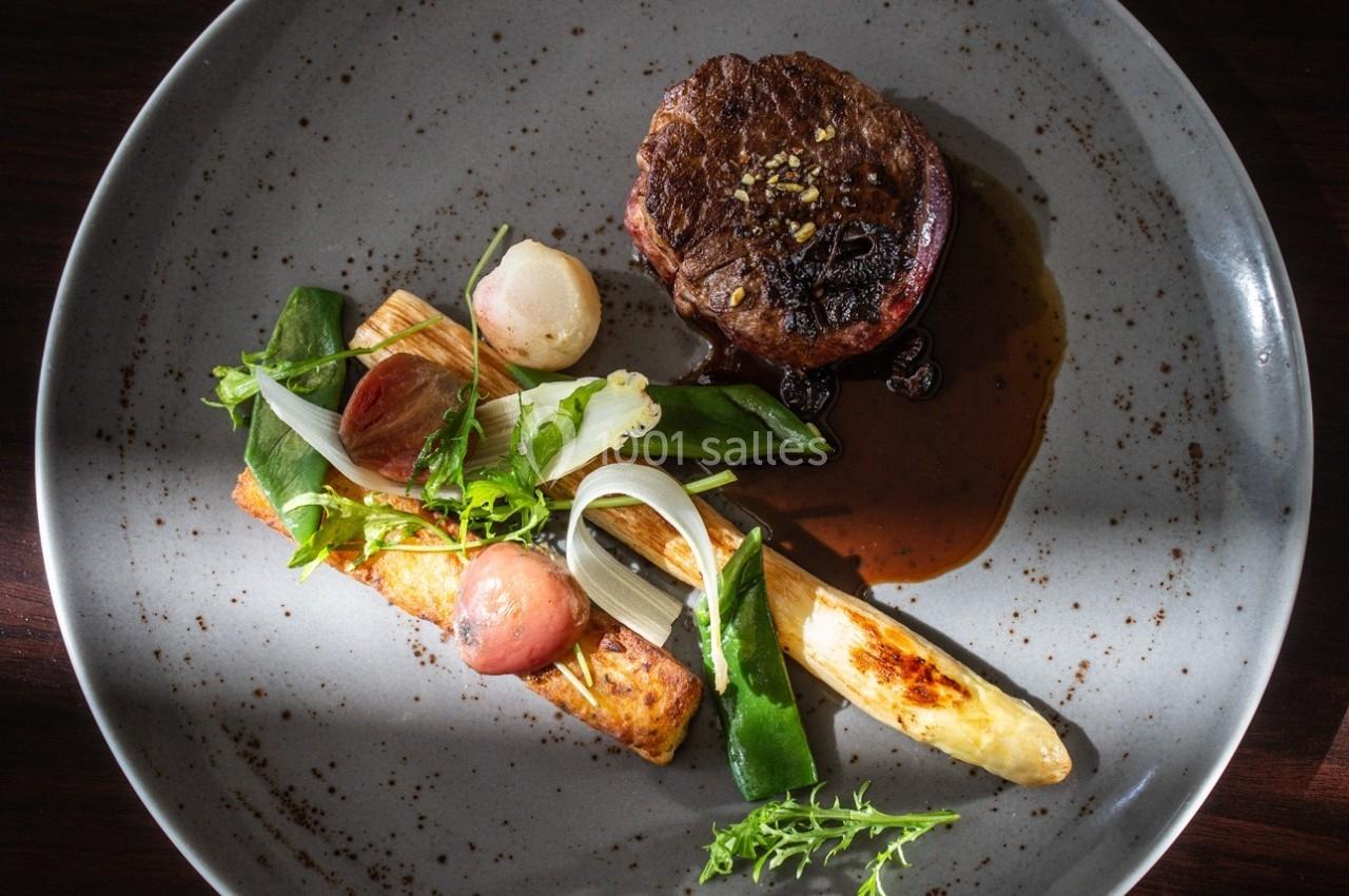 Assiette gastronomique avec un filet de viande, légumes variés et sauce, présentée sur une table sombre.
