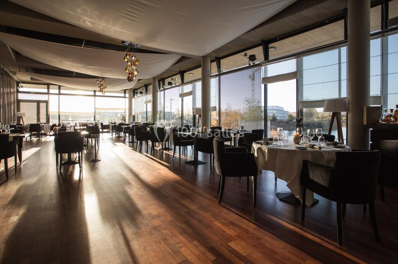 Salle de restaurant lumineuse avec de grandes baies vitrées, des tables dressées et un sol en parquet.