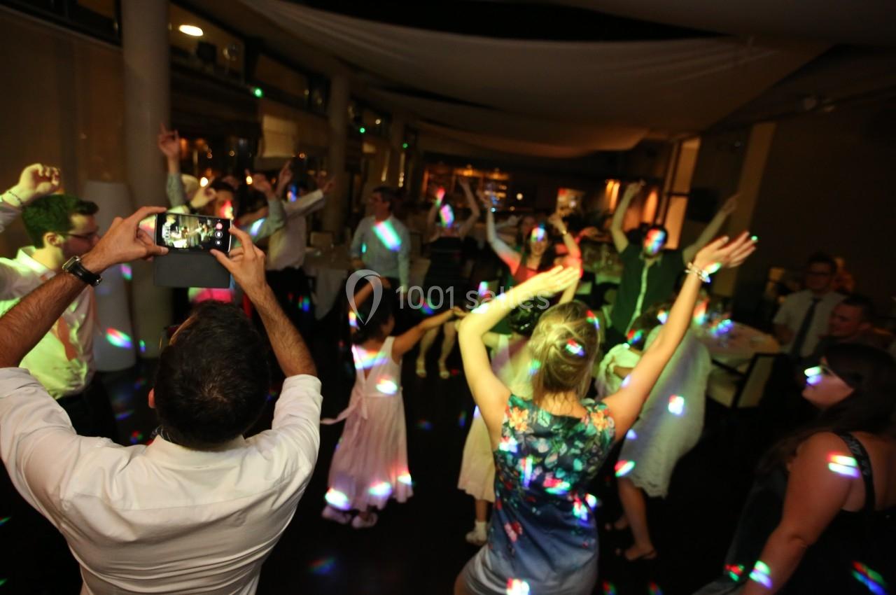 Personnes dansant sous des lumières colorées dans une salle sombre, avec un homme photographiant la scène.