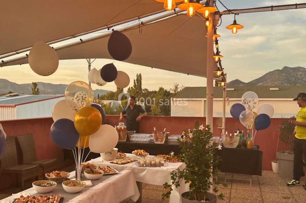 Terrasse décorée avec des ballons, tables garnies de plats et boissons, éclairage chaleureux au coucher du soleil.