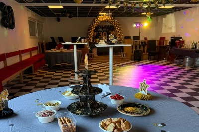 Terrasse extérieure couverte avec tables et chaises en osier, éclairée par des lumières suspendues, de nuit.