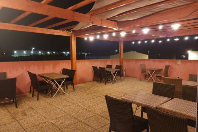 Terrasse extérieure couverte avec tables et chaises en osier, éclairée par des lumières suspendues, de nuit.