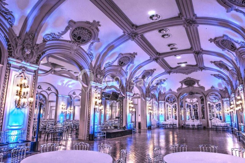 Salle de réception élégante avec hauts plafonds voûtés, lustres et éclairage bleu tamisé.