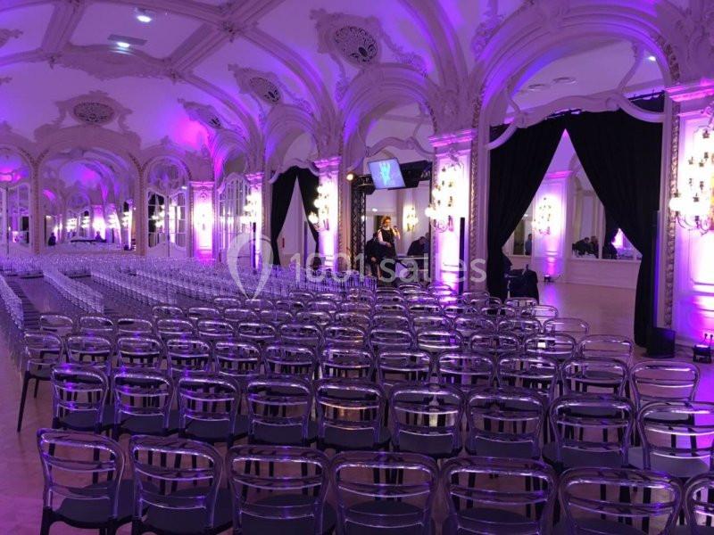 Salle de réception élégante avec des rangées de chaises transparentes, éclairage violet et rideaux noirs.