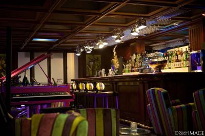 Salon avec fauteuils colorés, piano rose, bar en arrière-plan et décorations modernes dans une ambiance chaleureuse.