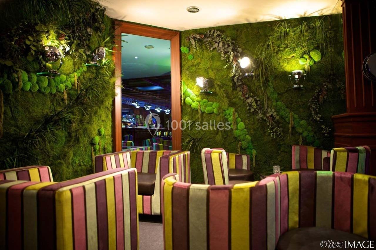 Fauteuils colorés dans un salon décoré de murs végétalisés avec un miroir reflétant un bar éclairé.