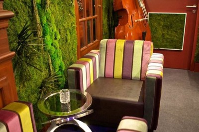 Salon avec fauteuils colorés, piano rose, bar en arrière-plan et décorations modernes dans une ambiance chaleureuse.