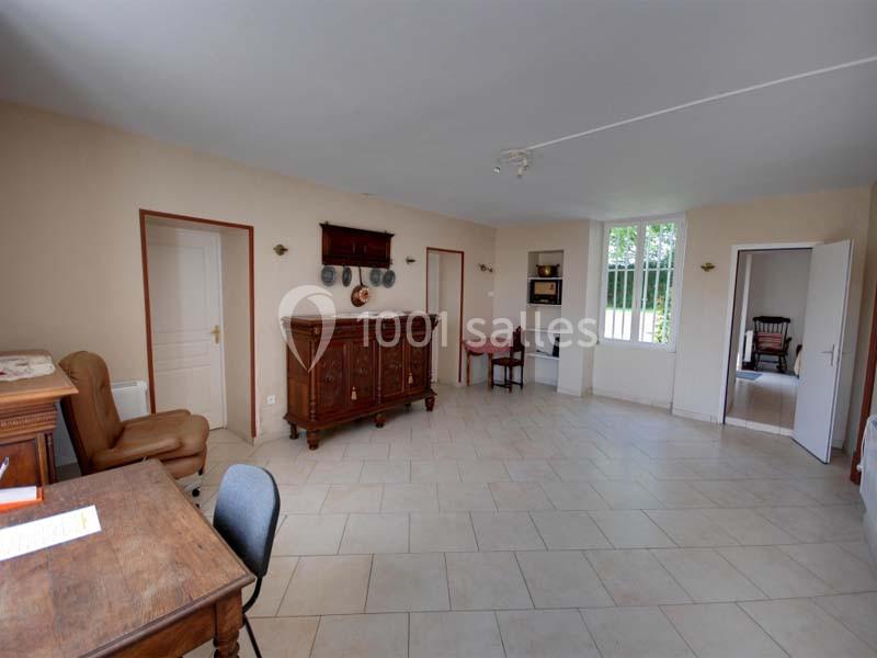 Salle de séjour lumineuse avec carrelage clair, meubles en bois, et vue sur une pièce adjacente avec une chaise à bascule.