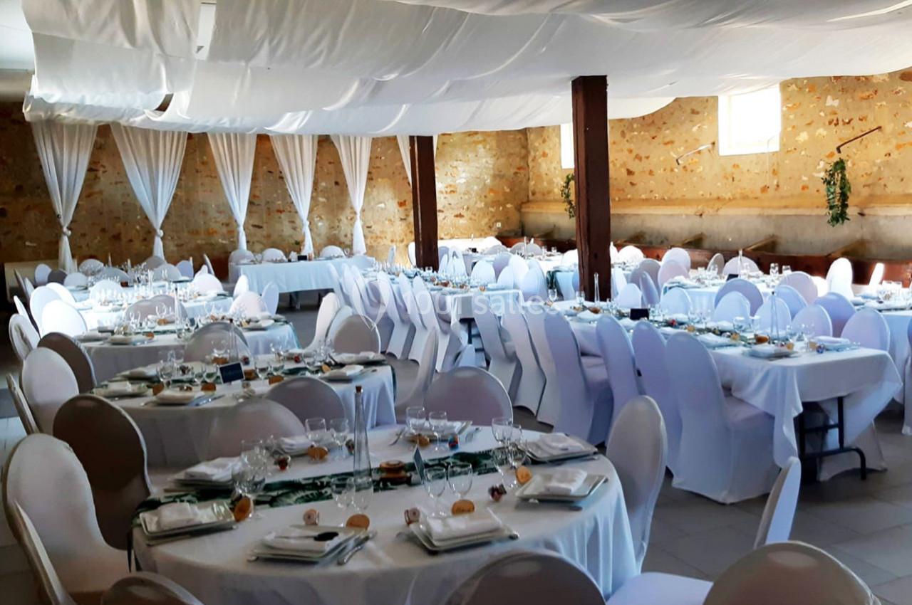 Salle de réception décorée avec des tables rondes dressées, nappes blanches et plafond drapé de tissu clair.