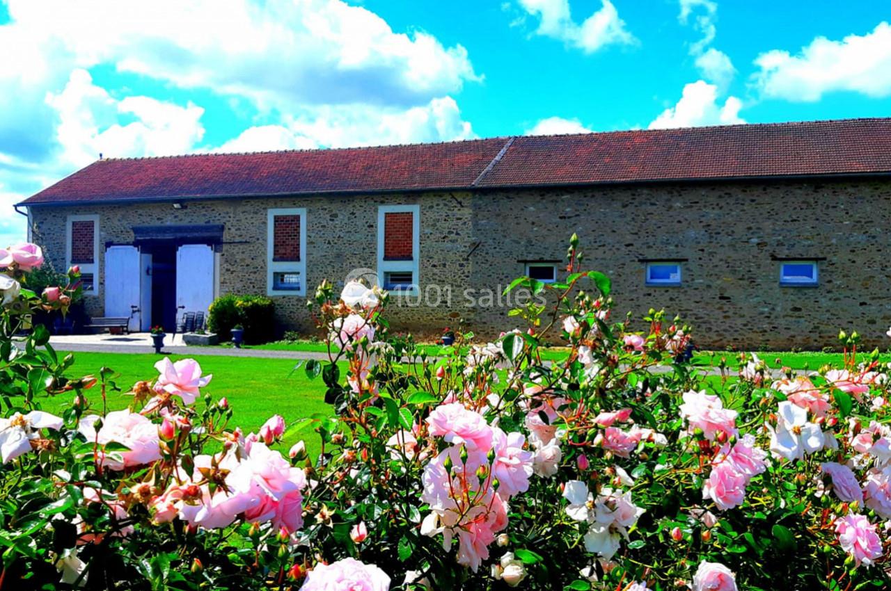 Bâtiment en pierre avec toit en tuiles rouges, entouré d'un jardin fleuri de roses sous un ciel bleu.