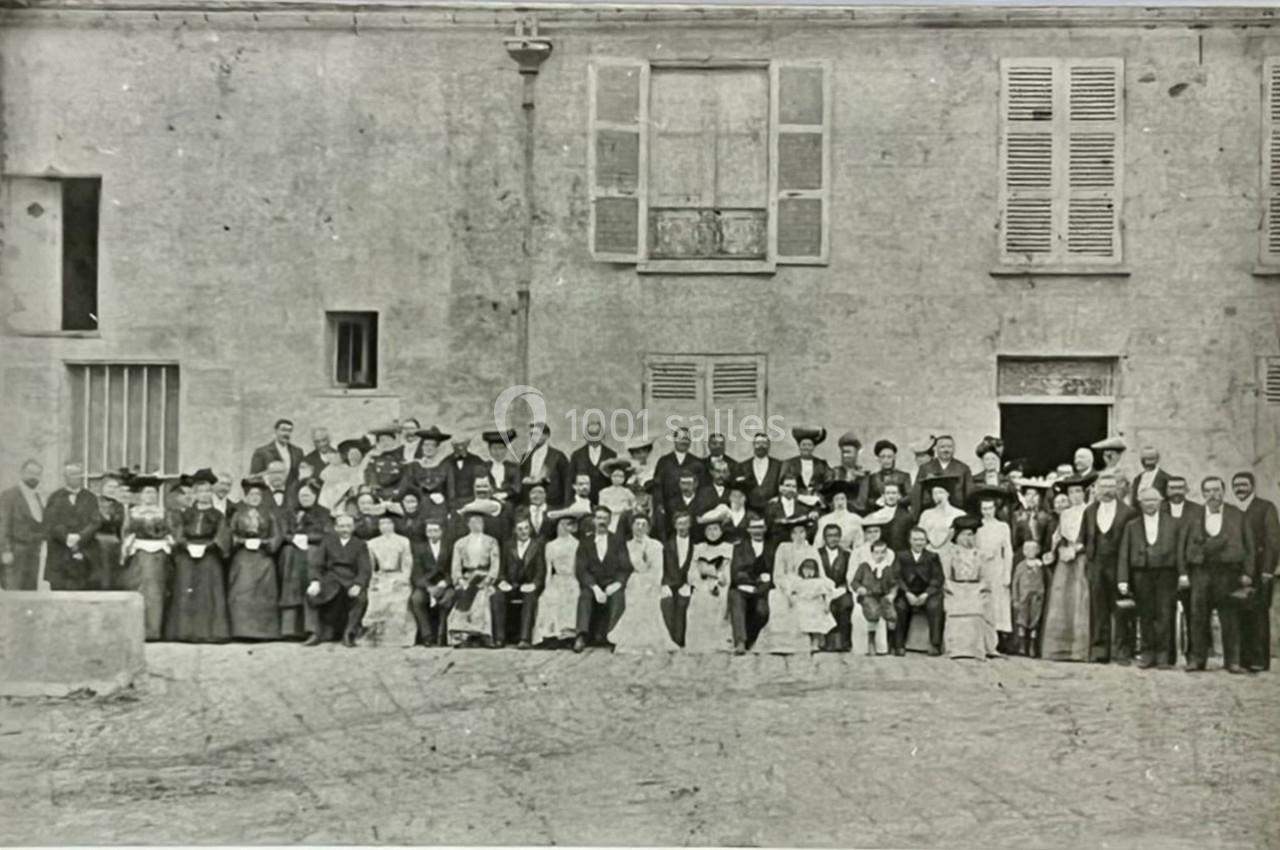 Photo en noir et blanc d'un grand groupe de personnes posant devant un bâtiment ancien avec des fenêtres et des volets.