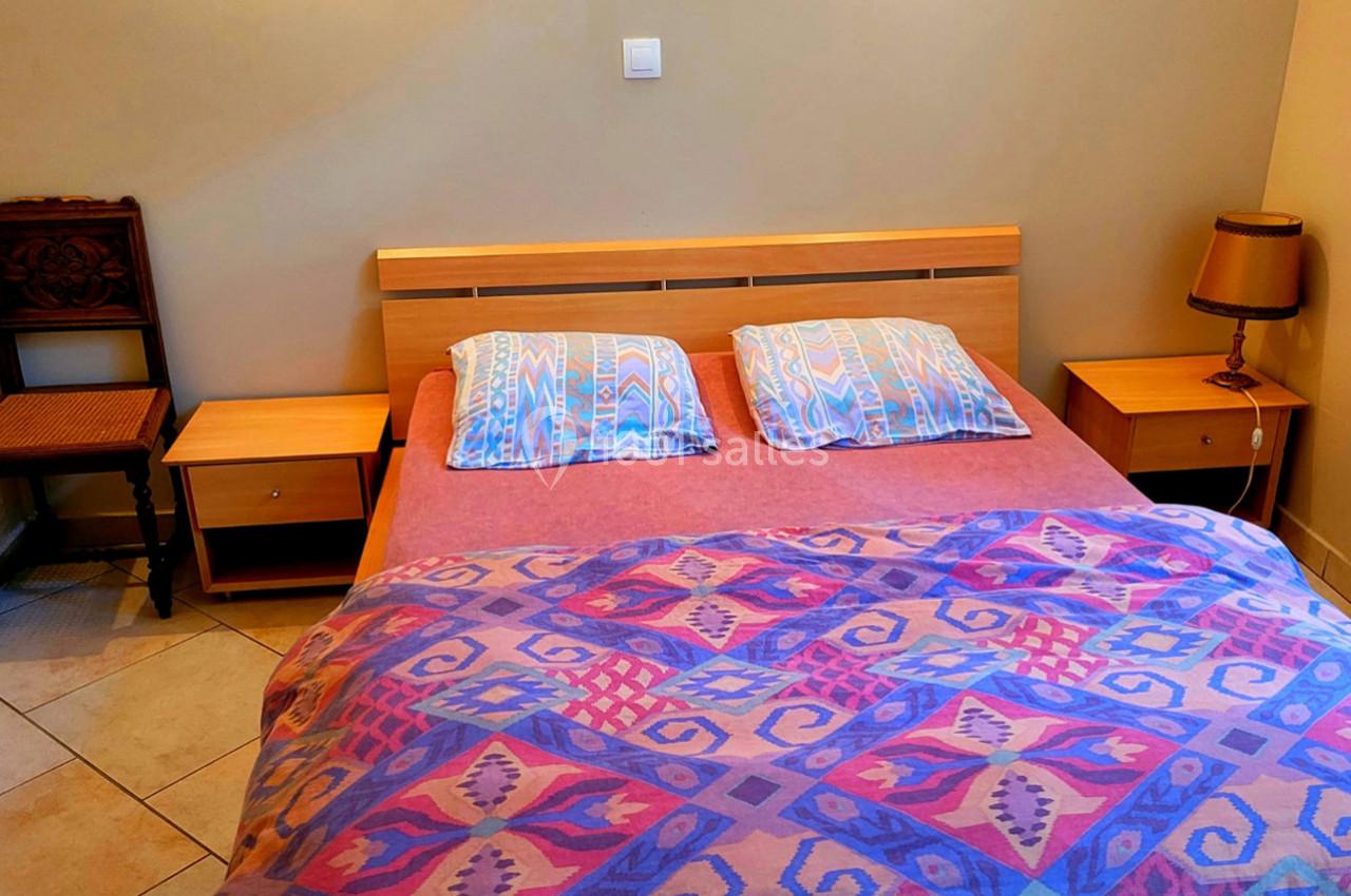 Lit double avec une couverture colorée, deux oreillers, tables de chevet en bois et une lampe dans une chambre simple.