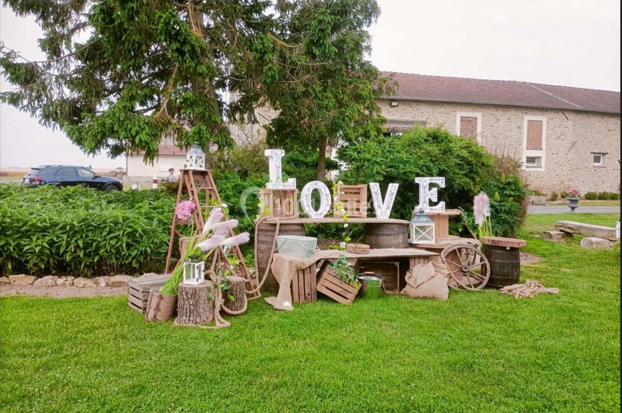 Décoration champêtre avec des lettres formant ’LOVE’, des caisses en bois, des lanternes et des fleurs sur une pelouse.