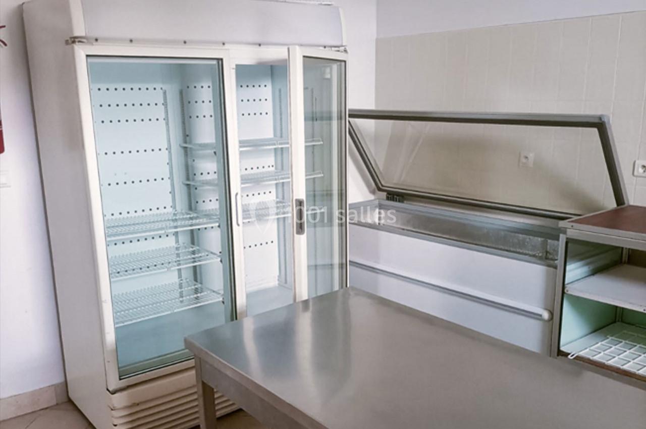 Deux réfrigérateurs professionnels vides dans une pièce carrelée avec une table en inox au premier plan.